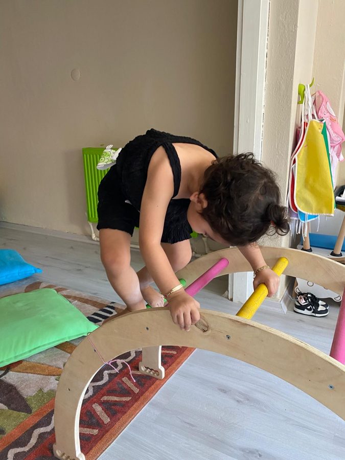 Çocuk, ahşap denge kemerinin renkli çubuklarını tutarak üzerinden geçiyor