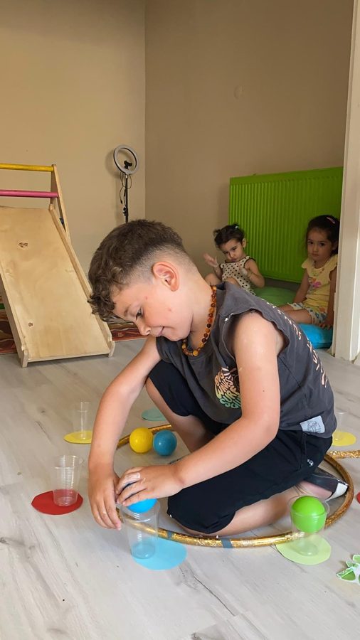 Çocuk, çemberin içindeki renkli topları bardaklara toplayarak el-göz koordinasyonu çalışıyor